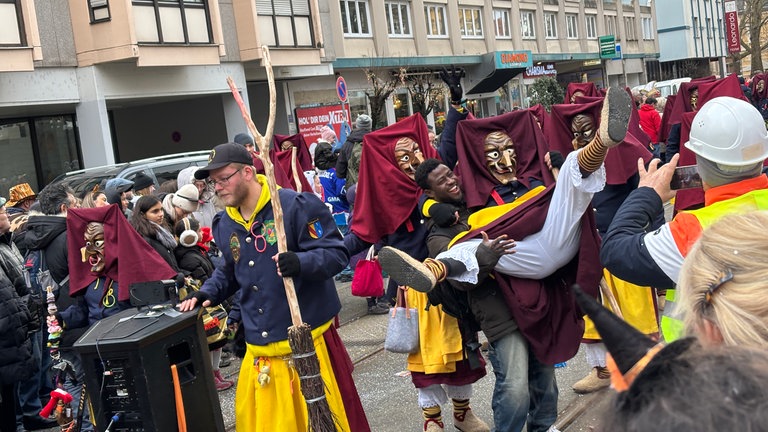 Ein Mann hebt eine Hexe mit Holzmaske hoch und nimmt sie auf den Arm