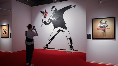 Eine Frau betrachtet das Wandbild "Flower Thrower" der Ausstellung "House of Banksy - An Unauthorized Exhibition" 