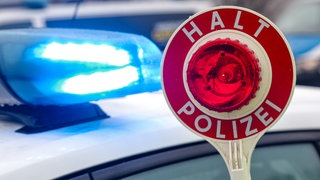 (Symbolbild) Eine Polizeikelle vor einem Streifenwagen mit Blaulicht