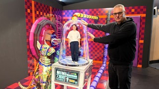 Der Betreiber des Museums, Guido Mülter, ist groß im Bild zu sehen, während seine Mitarbeiterin im Hintergrund ganz klein erscheint