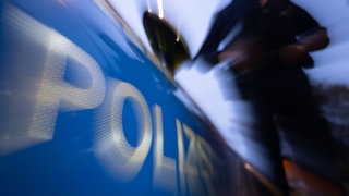 Eine Polizistin steht neben einem Polizeifahrzeug.