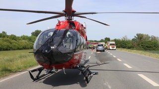 Blick auf eine Straße: Ein Hubschrauber der Luftrettung verdeckt einen Unfall im HIntergrund. Rettungskräfte stehen vor Ort. 