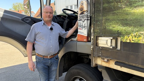 Ein Mann mit kurzärmeligem Hemd steht in der Fahrertür eines Lkw.