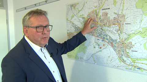 Mann mit Brille zeigt mit linker Hand auf eine Landkarte