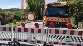 Straßenabsperrung und ein Baufahrzeug, im Hintergrund ein gelbes Ortsschild
