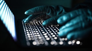 Mit handschuhen gekleidete Finger tippen auf einer Tastatur.
