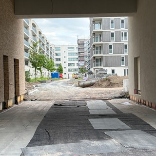 Ein offenes Baustellentor mit Blick in einen Hinterhof. Um ein großes Mehrstöckiges Gebäude steh ein Gerüst.
