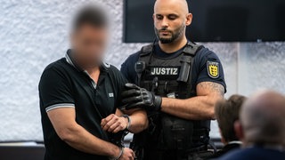Ein Justizbeamter führt den Angeklagten in Handschließen in einen Saal des Stuttgarter Landgerichts