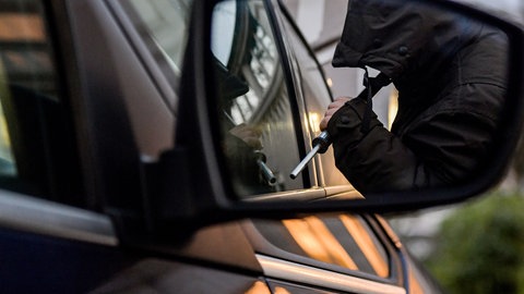 Ein Mann mit einer Brechstange steht am Fenster eines Autofensters.