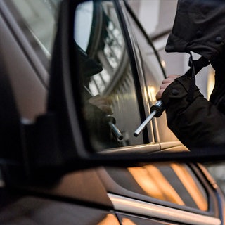 Ein Mann mit einer Brechstange steht am Fenster eines Autofensters.