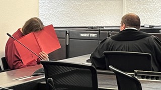 Angeklagter hält rote Mappe vor Gesicht: Nach Mord an Pflegeschülerin, muss Mann lebenslang ins Gefängnis.