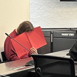 Angeklagter hält rote Mappe vor Gesicht: Nach Mord an Pflegeschülerin, muss Mann lebenslang ins Gefängnis.