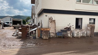 Schlammiger Hausrat steht in Rudersberg (Rems-Murr-Kreis) nach der Flut auf der Straße. (Archivbild)