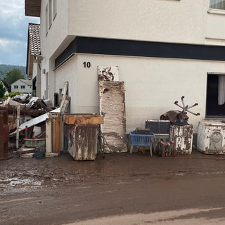 Schlammiger Hausrat steht in Rudersberg (Rems-Murr-Kreis) nach der Flut auf der Straße. (Archivbild)