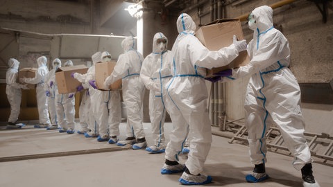 Polizisten in Schutzkleidung schaffen Kartons voller Kokain zur Zuführung der Brennkammer eines Müllheizkraftwerks.