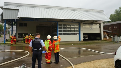 Feuerwehrleute und ein Polizist stehen bei einem Feuerwehreinsatz vor einer Werkstatt in Geislingen an der Steige (Kreis Göppingen). 