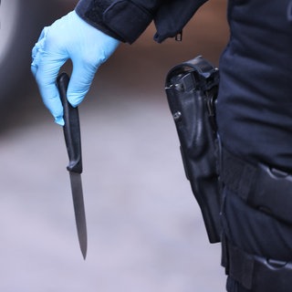 Zwei Polizisten, die beide Handschuhe haben. Einer der beiden trägt ein Messer in der Hand mit der spitzen Seite nach unten.