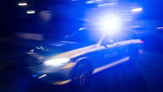 Ein Polizeiauto fährt bei Nacht mit Blaulicht an einem Gebäude vorbei (Archivbild).