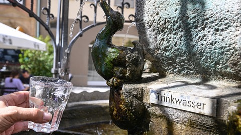 Am Hans-Im-Glück-Trinkwasserbrunnen in der Stuttgarter Innenstadt wird ein Glas Wasser mit Trinkwasser gefüllt.