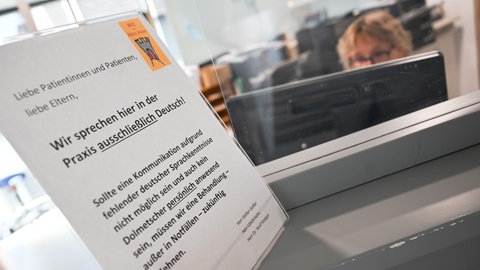 Ein Schild mit der Aufschrift "Wir sprechen hier in der Praxis ausschließlich Deutsch" steht auf einem Tresen an dem Empfangsbereich einer Praxis für Kinder- und Jugendmedizin in Kirchheim unter Teck.