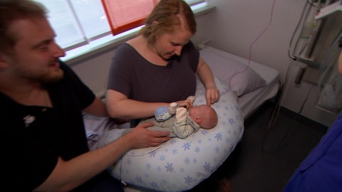 Melanie und Markus Ostermann sitzen auf einem Krankenhausbett und kümmern sich um ihr Kind, ein Frühchen.