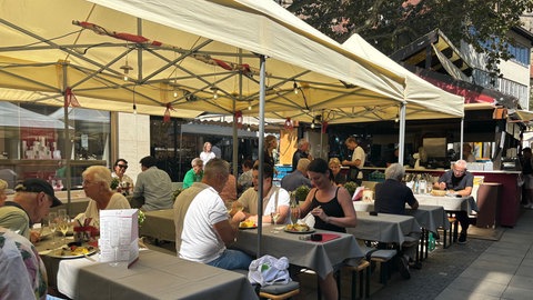 Erster Tag auf dem Stuttgarter Weindorf 2024: Am Mittag lassen sich schon einige Besucher und Besucherinnen die regionalen Leckereien schmecken.