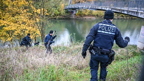 Mehrere Einsatzkräfte der Polizei durchkämmen das hohe Gras am Neckarufer.