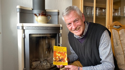 Christian Siller, Direktor der Holz-Heiz-Akademie, sitzt vor einem Kaminofen und hält eine Borschüre zum Heizen in der Hand