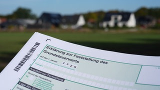 Eine Erklärung zur Feststellung des Grundsteuerwerts für das Jahr 2025 wird vor eine Wohnsiedlung hochgehalten: Wendingen am Neckar führt die Grundsteuer C ein. (Symbolbild)