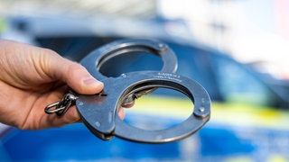 Symbolbild von Handschellen: Eine junge Frau sitzt in U-Haft, weil sie die Getränke von Kollegen mit Medikamenten versetzt haben soll.