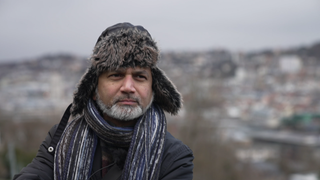 Faisal Khan trägt eine Fellmütze und eine Winterjacke. Er steht auf der Karlshöhe in Stuttgart, hinter ihm sieht man die Stadt.