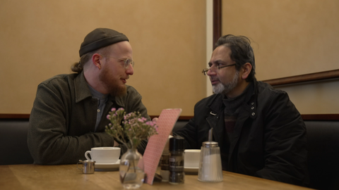 Sozialpädagoge Lukas Müller von der Suchtberatung "Al-Mudmin" sitzt gemeinsam mit Faisal Khan in einem Café. Die beiden unterhalten sich.