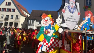 Auf dem vordersten Wagen beim Fasnetumzug 2025 in Donzdorf steht: "66. Donzdorfer Fasnetumzug". Der Wagen ist mit Clowns bemalt und am Straßenrand stehen viele Zuschauerinnen und Zuschauer.
