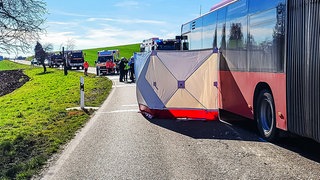 Ein Sichtschutz ist nach einem Unfall an einem Bus zu sehen, während Helfer im Einsatz sind. 