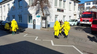 Feuerwehrkräfte in Schutzanzügen stehen vor einem Gebäude.