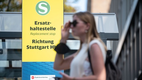 Eine Frau steht in Stuttgart vor einem Hinweisschild zu Schienenersatzverkehr: Die Fahrgäste müssen sich im Sommer mit einigen Unannehmlichkeiten rechnen. (Archivbild)