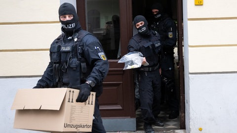 Vermummte Polizisten tragen Beweismaterial nach einer Razzia aus dem Haus. (Symbolbild)
