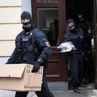 Vermummte Polizisten tragen Beweismaterial nach einer Razzia aus dem Haus. (Symbolbild)