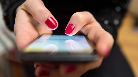 Eine Person tippt mit beiden Händen auf ihr Handy, Fingernägel sind rot lackiert. Ein Mann aus dem Rems-Murr-Kreis ist auf sogenanntes "Love Scamming" auf einer Dating Plattform reingefallen. Laut dem Polizeipräsidium Aalen hat er einer Person, die sich online als Notärztin ausgegeben hat, rund 2,3 Millionen Euro überwiesen. Kurz nach dem er das Geld überwiesen habe, brach die betrügerische Person den Kontakt ab. 