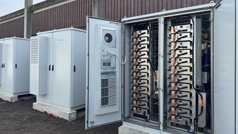 Drei große Batteriespeicher-Kästen, einer davon ist geöffnet und zeigt die verkabelten Batterien.