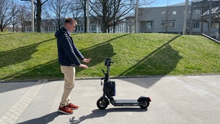 Doktorand Robin Strässer mit einem Prototypen des autonom fahrenden E-Scooters auf dem Campus der Universität Stuttgart