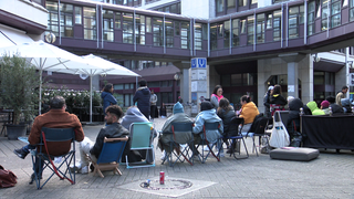 Menschen warten mit Kissen und Stühlen vor der Ausländerbehörde Stuttgart. (Archivbild)