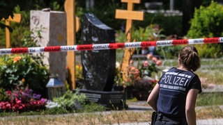 Eine Polizistin geht über den abgesperrten Teil an einem Tatort auf einem Friedhof. (Archivbild) Nach dem Handgranaten-Wurf im Kreis Esslingen kommt der Fall eines mutmaßlich Beteiligten wieder vors Stuttgarter Landgericht.