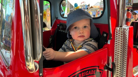 Ein Kleinkind sitzt in einem Feuerwehrauto auf einem Kinderkarussell. 