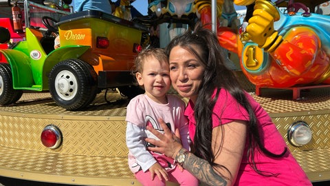 Ein Kleinkind mit seiner Mutter vor einem Kinderkarussell.