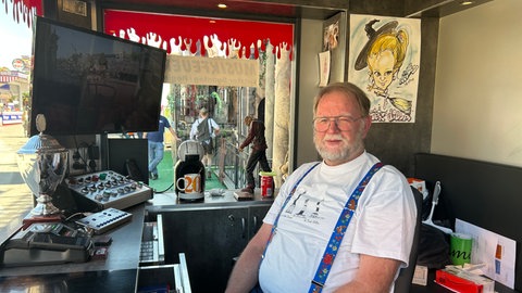 Ein Schausteller sitzt hinter der Kasse der Geisterbahn. 