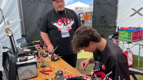Claus und sein Sohn Jonas sitzen in einem Zelt beim Drone Championship und basteln an ihren Drohnen. Sie bauen ihre Drohnen selbst.