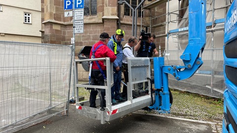 In Stuttgart-Bad Cannstatt wird ein Team mit einem Kran hoch zur renovierten Kirchturmspitze gehoben.