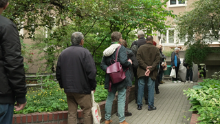 Vor dem Hilfsangebot "eva's Tisch" stehen Menschen, die von Armut betroffen sind. Sie stehen in einer Schlange für ein warmes Mittagessen.