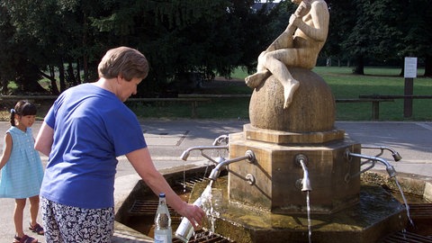 Eine Dame füllt sich am öffentlichen Brunnen im Kurpark von Stuttgart-Bad Cannstatt Mineralwasser in mitgebrachte Flaschen. 